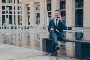 Successful businessman talking on mobile phone while working outside, sitting on bench